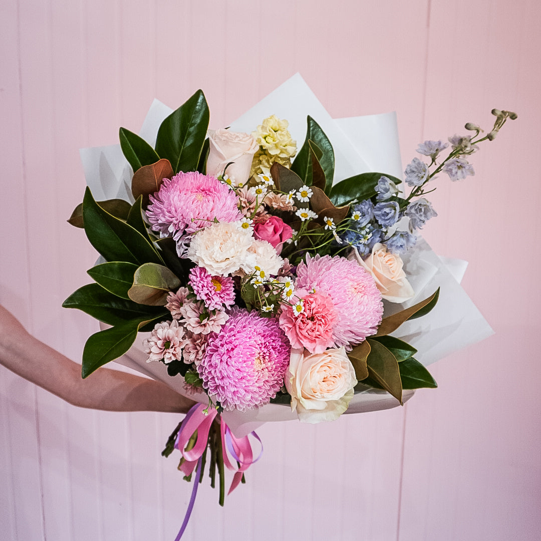 An extra large bouquet of flowers by Taylor Made Blooms, held by a person against a pink background
