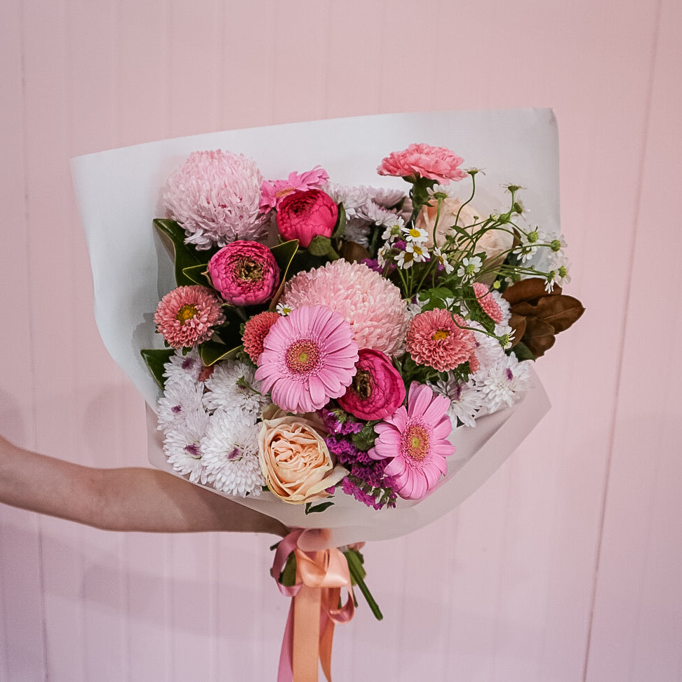 A bouquet of flowers by Taylor Made Blooms held by a florist against a pink background.