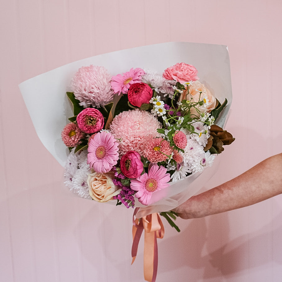 Bouquet of flowers by Taylor Made Blooms held by a person against a pink background