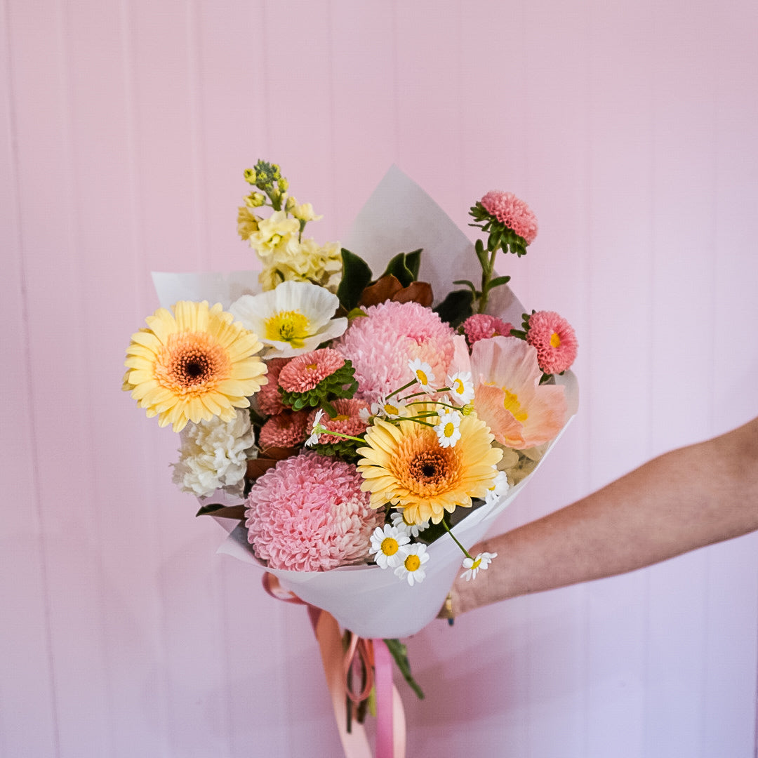 A bouquet of flowers by Taylor Made Blooms held by a person against a pink background.