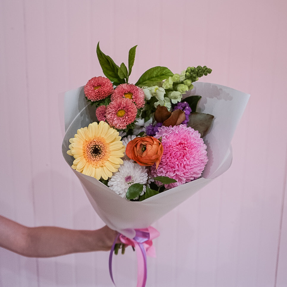 A bouquet of colourful flowers by Taylor Made Blooms held against a pink background.