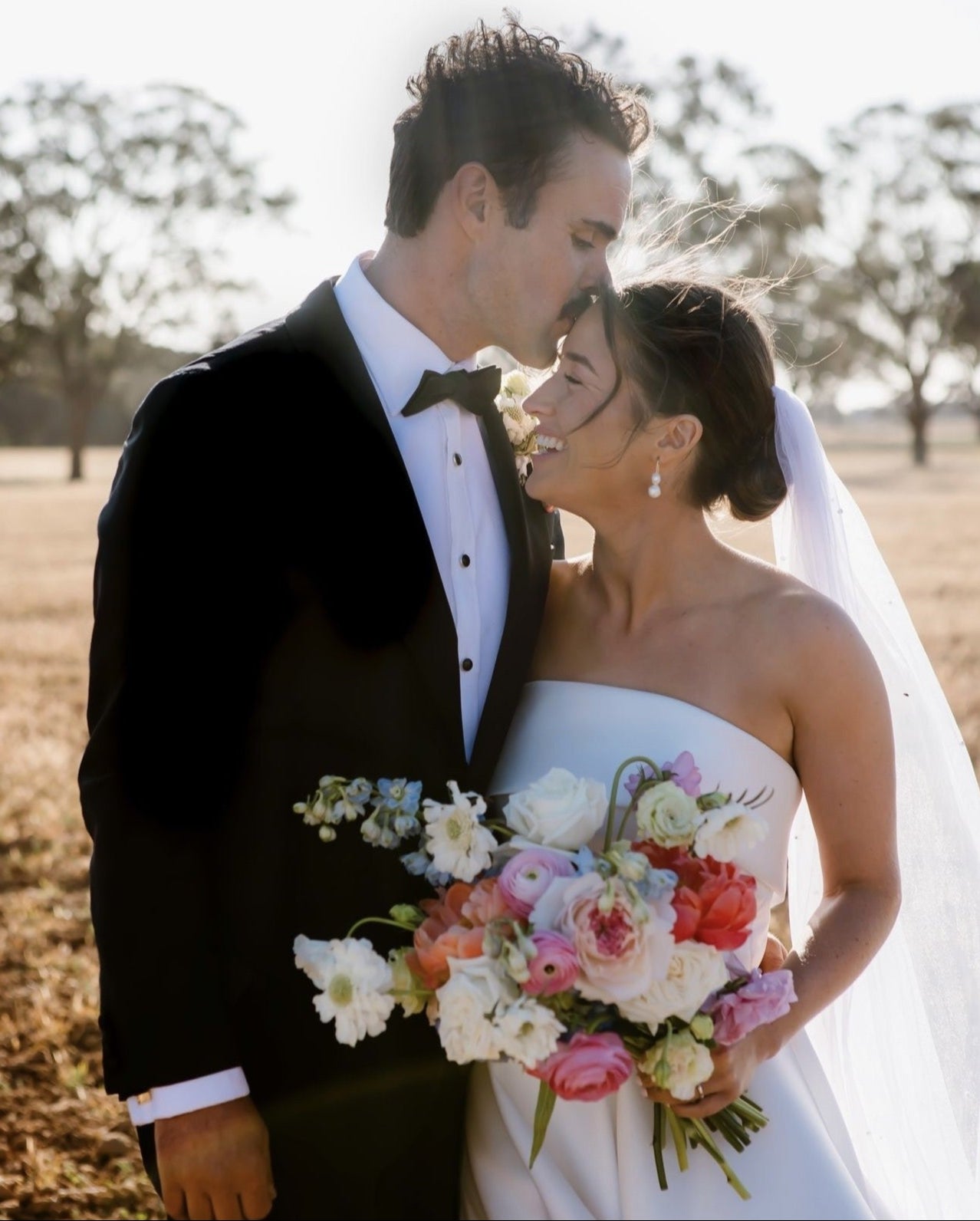 A happy couple celebrating their marriage. The bride is holding a beautiful custom-made bouquet from Taylor Made Blooms.