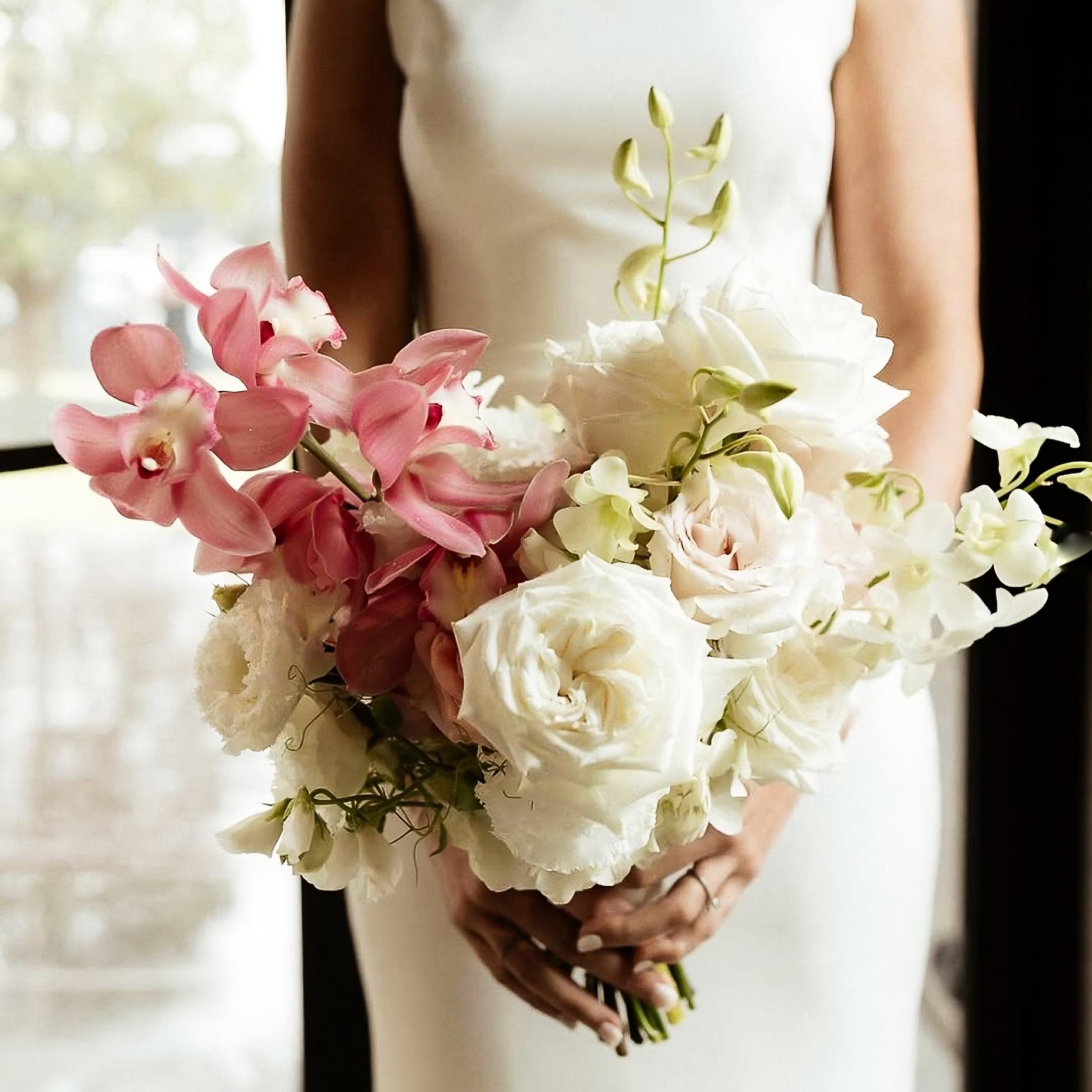 Bouquet of pink and white flowers held by a person in a white wedding dress.