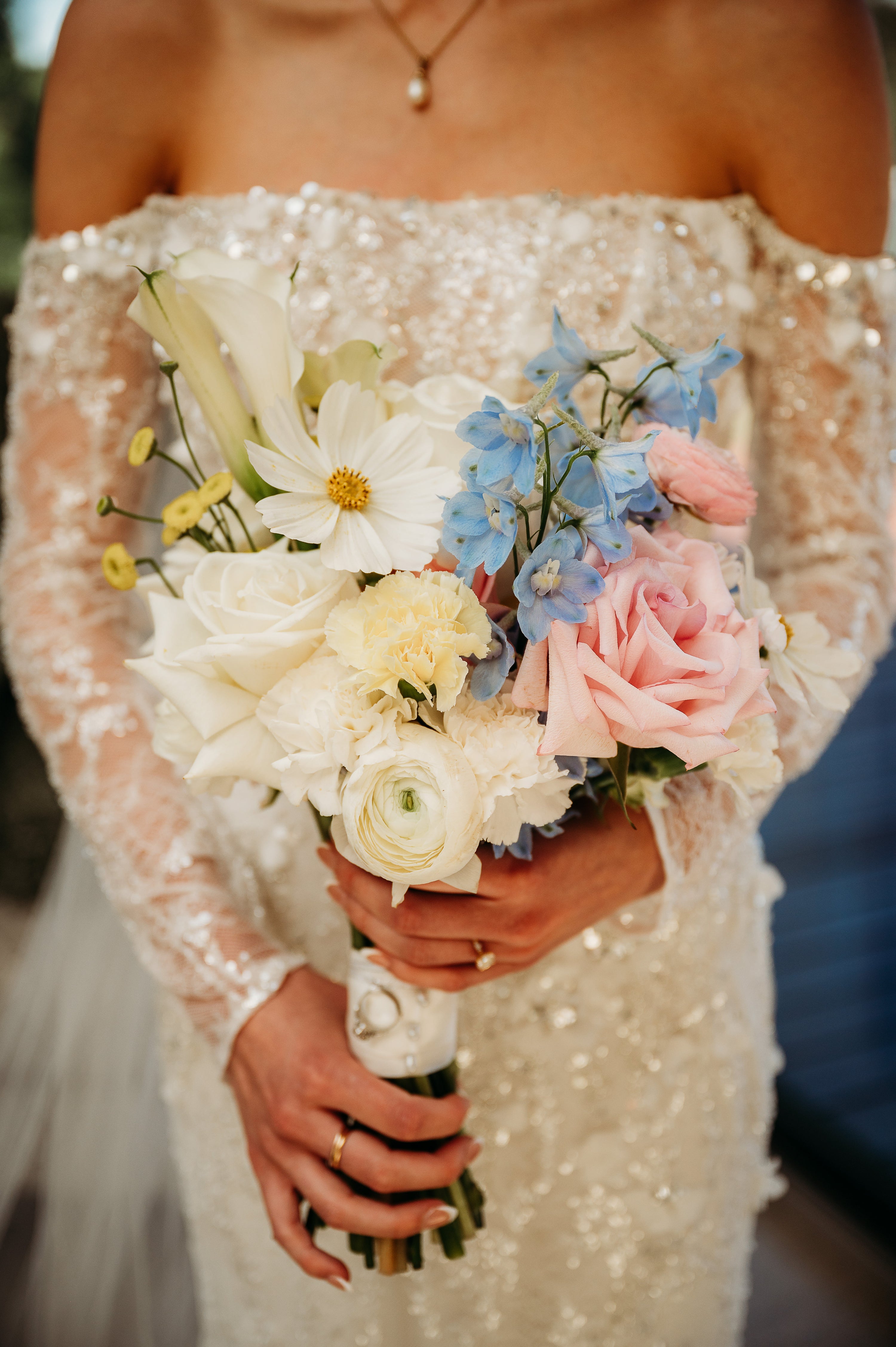Bride holding a bouquet of flowers by Taylor Made Blooms in a white dress with lace details.